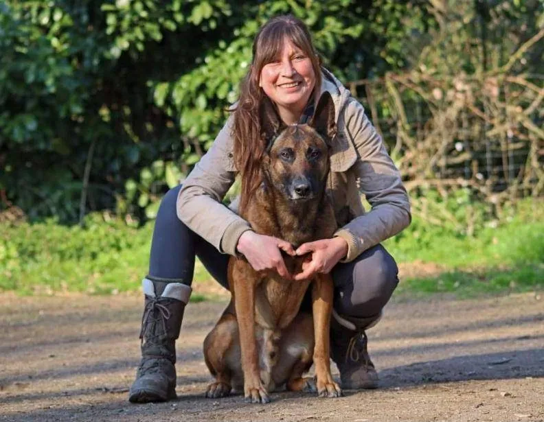 Lynn hockt lachend hinter ihrem Malinois